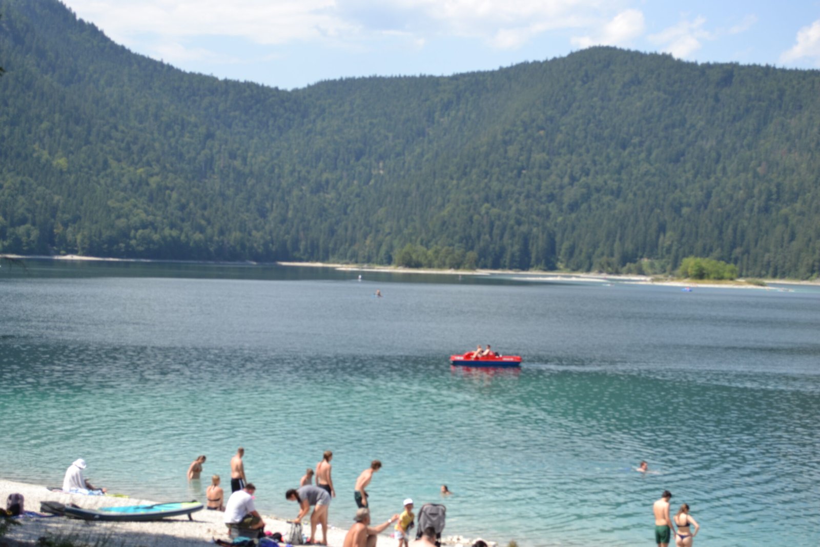 Swimmers and a red boat on the blue water of Eibsee